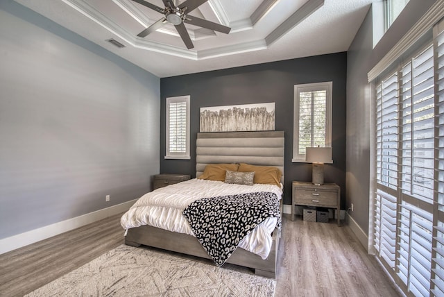 bedroom featuring coffered ceiling, wood finished floors, visible vents, baseboards, and crown molding