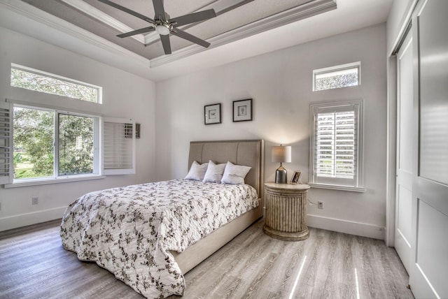 bedroom featuring light wood-style floors, a tray ceiling, crown molding, and baseboards