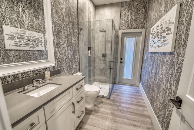 bathroom with toilet, wallpapered walls, a shower stall, and vanity