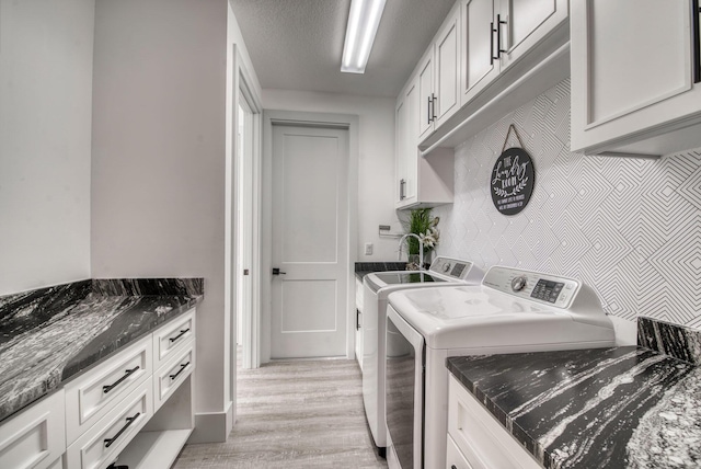 laundry area featuring cabinets, light wood-type flooring, a textured ceiling, and independent washer and dryer