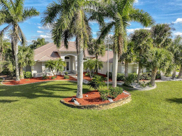 mediterranean / spanish-style home with a front yard, a tiled roof, and stucco siding