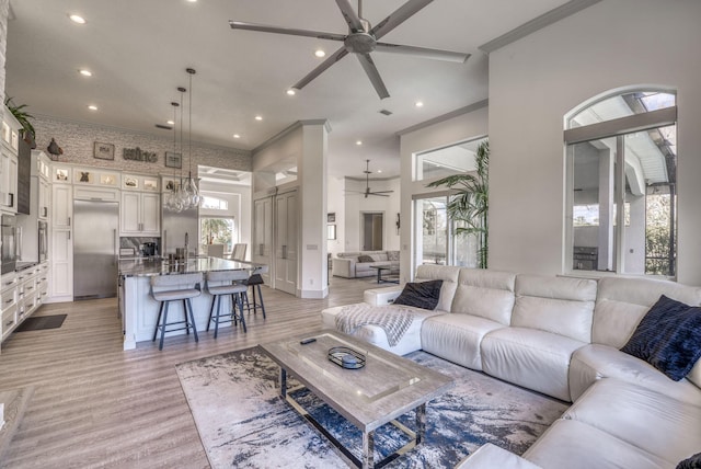 living room featuring ceiling fan, a barn door, light wood-style flooring, recessed lighting, and ornamental molding