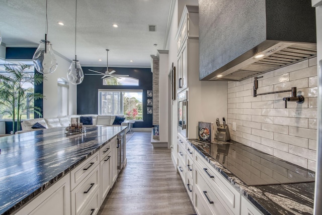 kitchen featuring decorative light fixtures, crown molding, white cabinetry, wood finished floors, and dark stone counters