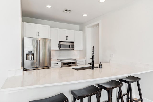 kitchen featuring sink, kitchen peninsula, a kitchen bar, white cabinets, and appliances with stainless steel finishes