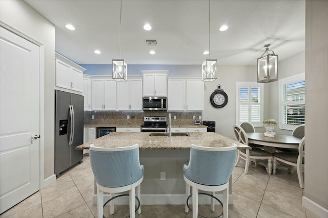 kitchen featuring white cabinets, appliances with stainless steel finishes, a center island with sink, and hanging light fixtures