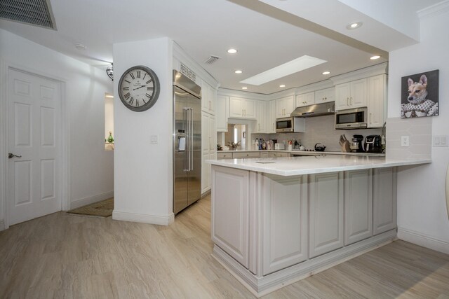 kitchen with built in appliances, white cabinetry, sink, and range hood