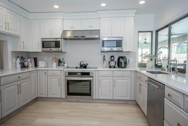 kitchen with kitchen peninsula, appliances with stainless steel finishes, tasteful backsplash, white cabinets, and range hood