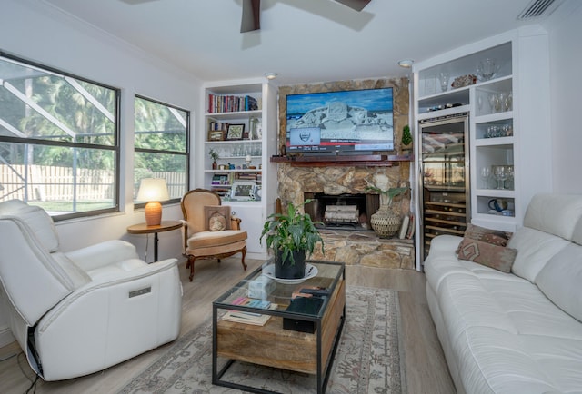 living room featuring wine cooler, built in shelves, light hardwood / wood-style flooring, and a stone fireplace