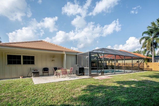 rear view of property with a lawn, glass enclosure, a fenced in pool, and a patio