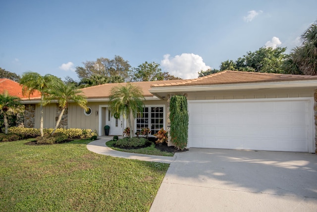 ranch-style house with concrete driveway, a front yard, an attached garage, and a tile roof
