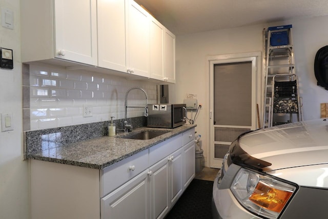 kitchen featuring white cabinets, backsplash, dark stone countertops, and sink