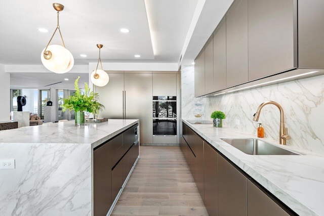 kitchen with pendant lighting, gray cabinets, light stone counters, and sink