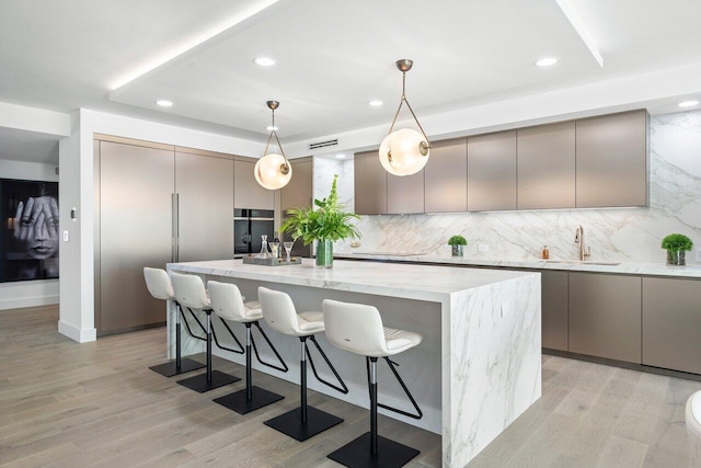 kitchen featuring pendant lighting, a kitchen island with sink, sink, tasteful backsplash, and light hardwood / wood-style floors