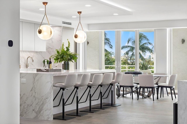 kitchen featuring white cabinets, light hardwood / wood-style flooring, decorative light fixtures, a kitchen bar, and kitchen peninsula