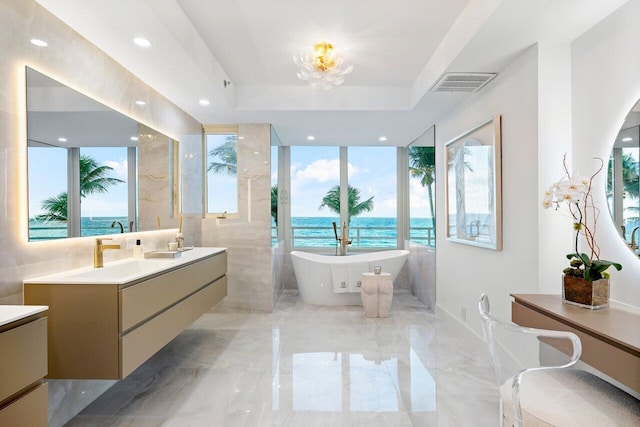 bathroom with vanity, a water view, a tub, and a tray ceiling