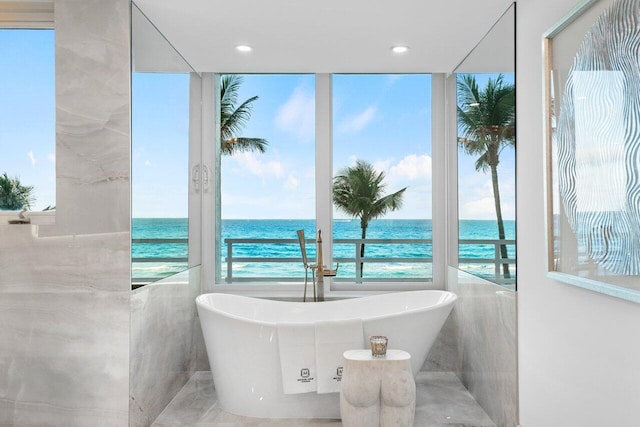 bathroom featuring a view of the beach, a bath, a water view, and tile walls