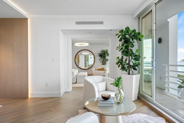 hall with a wealth of natural light, light hardwood / wood-style floors, and an inviting chandelier