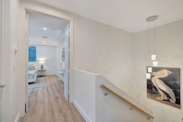 hallway with an upstairs landing, light wood-type flooring, visible vents, and baseboards