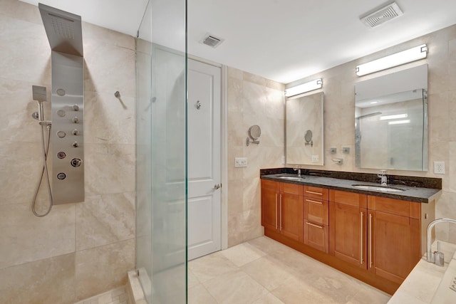 bathroom with visible vents, tile walls, walk in shower, and a sink