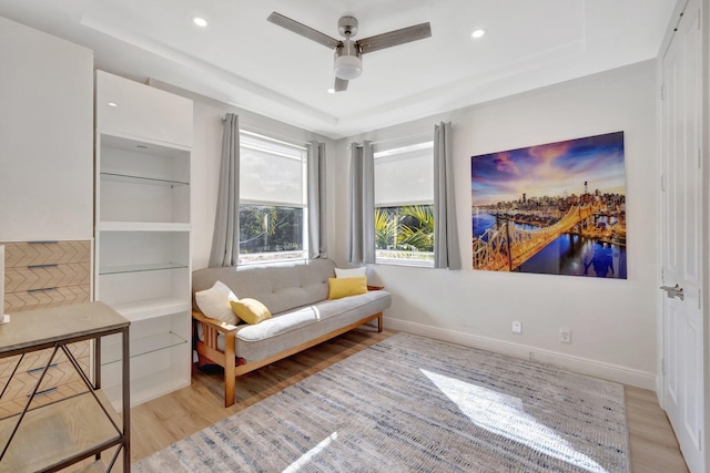 sitting room with built in shelves, ceiling fan, a tray ceiling, and light wood-type flooring