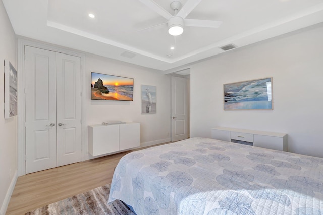 bedroom featuring ceiling fan, light hardwood / wood-style flooring, a closet, and a raised ceiling