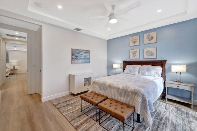 bedroom featuring light wood-type flooring, a raised ceiling, visible vents, and baseboards