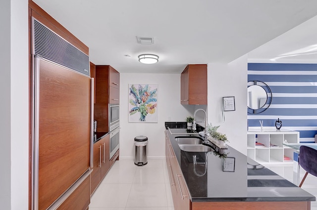 kitchen featuring built in appliances, sink, and light tile patterned flooring