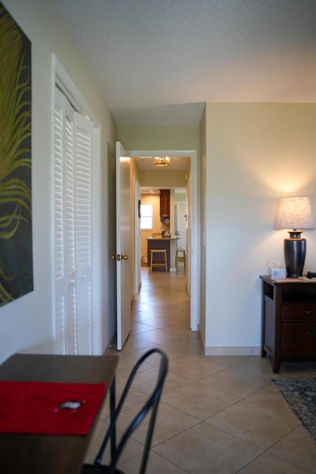 corridor featuring light tile patterned floors, a textured ceiling, and an inviting chandelier