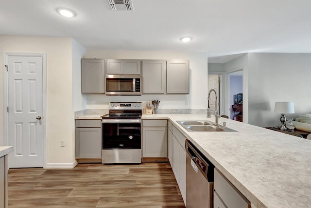 kitchen with gray cabinetry, sink, light wood-type flooring, and appliances with stainless steel finishes