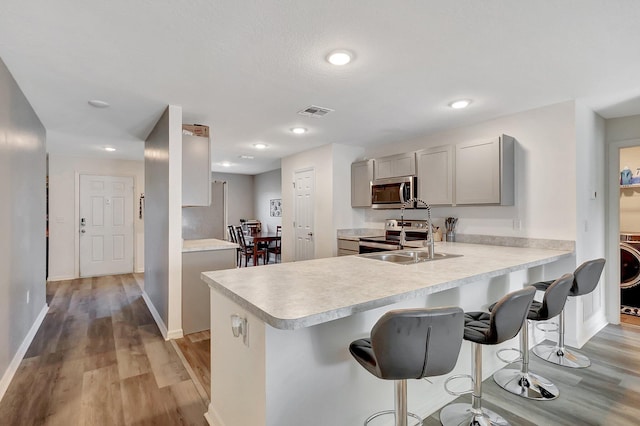 kitchen with gray cabinetry, a kitchen breakfast bar, light wood-type flooring, appliances with stainless steel finishes, and kitchen peninsula