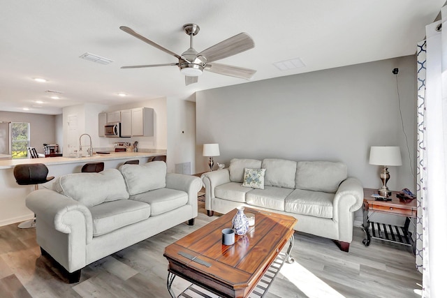 living room featuring light wood-type flooring, ceiling fan, and sink