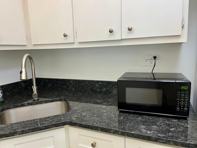 interior details with white cabinets, dark stone countertops, and sink