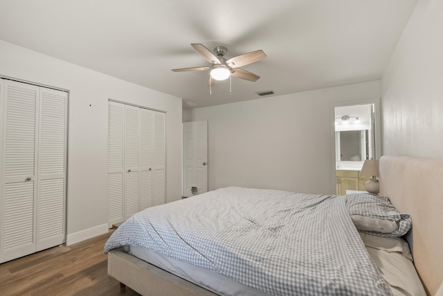 bedroom featuring dark hardwood / wood-style flooring, ensuite bathroom, ceiling fan, and multiple closets