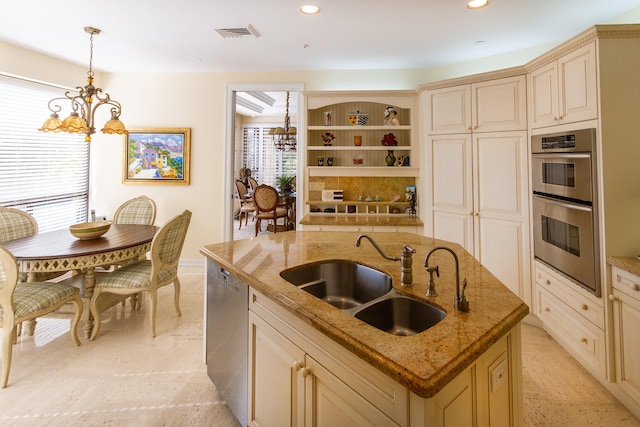 kitchen featuring a center island with sink, sink, light stone countertops, appliances with stainless steel finishes, and decorative light fixtures