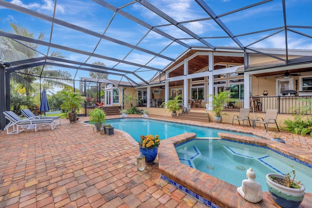 view of swimming pool featuring glass enclosure, ceiling fan, a patio area, and an in ground hot tub