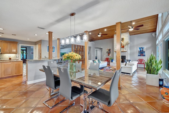 dining area with ceiling fan, light tile patterned flooring, a stone fireplace, and wooden ceiling