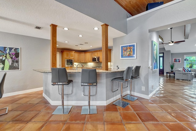 kitchen with kitchen peninsula, a kitchen breakfast bar, stainless steel appliances, and vaulted ceiling