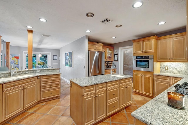 kitchen featuring a center island, sink, decorative backsplash, light stone countertops, and appliances with stainless steel finishes