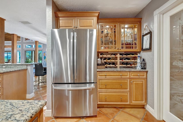 kitchen featuring stainless steel refrigerator, light stone countertops, light tile patterned floors, and a textured ceiling