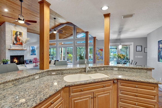 kitchen with a large fireplace, sink, light stone counters, a textured ceiling, and wood ceiling