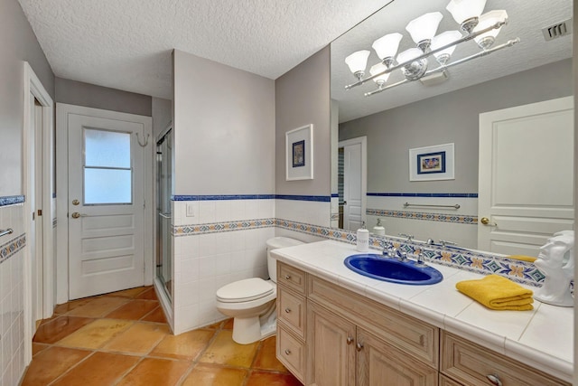 bathroom with vanity, tile patterned flooring, toilet, a textured ceiling, and tile walls