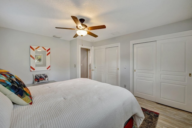 bedroom featuring a textured ceiling, ceiling fan, light hardwood / wood-style floors, and two closets