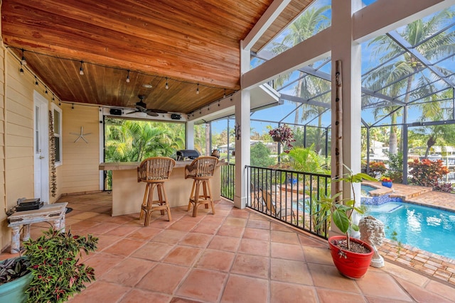 view of patio featuring glass enclosure, ceiling fan, and exterior bar