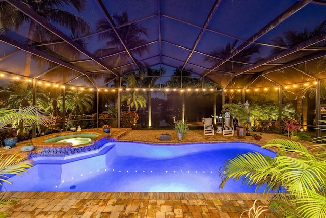 pool at night with glass enclosure and an in ground hot tub