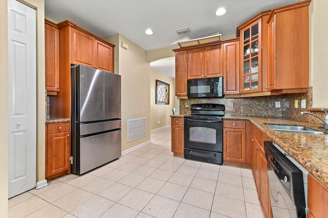 kitchen with sink, tasteful backsplash, light stone counters, light tile patterned flooring, and black appliances