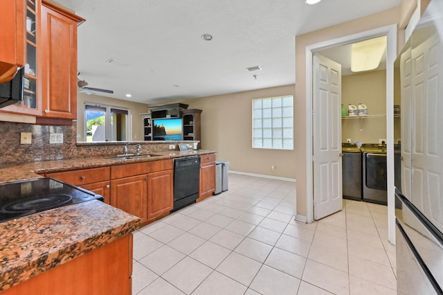 kitchen featuring sink, decorative backsplash, light tile patterned floors, black dishwasher, and washing machine and clothes dryer