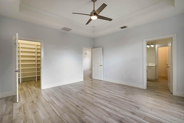 unfurnished bedroom with a spacious closet, a closet, ceiling fan, a tray ceiling, and crown molding