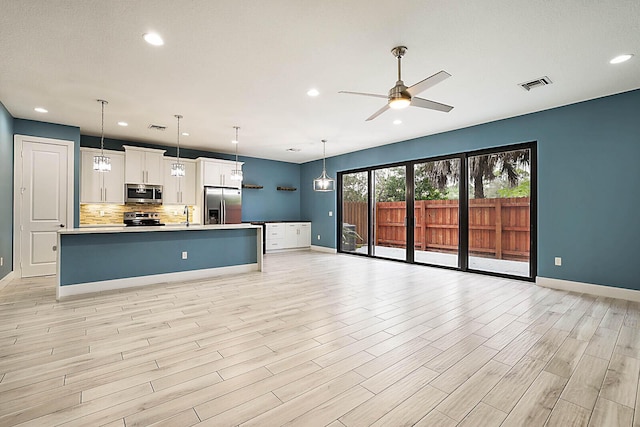 kitchen featuring decorative light fixtures, an island with sink, white cabinets, and appliances with stainless steel finishes