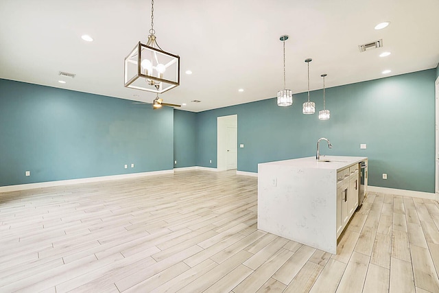 kitchen with hanging light fixtures, sink, white cabinetry, a center island with sink, and light hardwood / wood-style floors