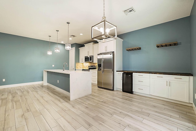 kitchen with appliances with stainless steel finishes, decorative light fixtures, white cabinetry, wine cooler, and backsplash